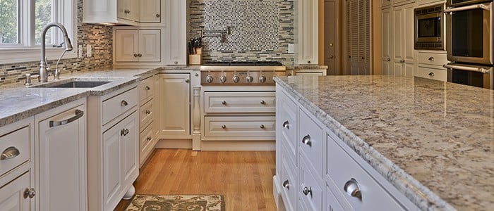 a kitchen remodel with brown granite countertops, white cabinets, and a range stove with tile backsplash and a pot filler