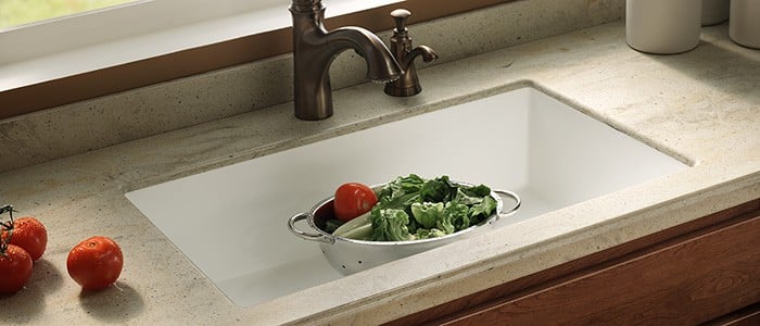 close up of a solid surface countertop with a large white sink and vegetables in a strainer