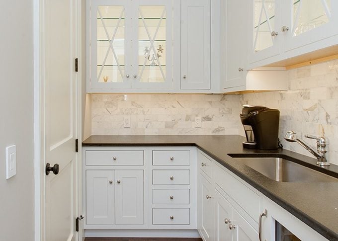 butlers pantry with white cabinets and black granite countertops