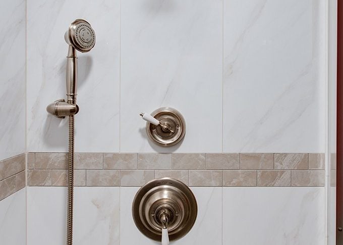 white marble tile area with stainless finish shower head and handle