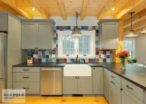 Painted light green craftsman kitchen with white farmers sink and patchwork backsplash tile