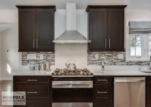 Dark maple kitchen showing quartz countertop up behind stove area and decorative tile everywhere else for backsplash