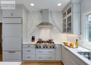 Light Grey kitchen with stainless cooktop and modern stainless hood, with white Cambria on wall up to ceiling