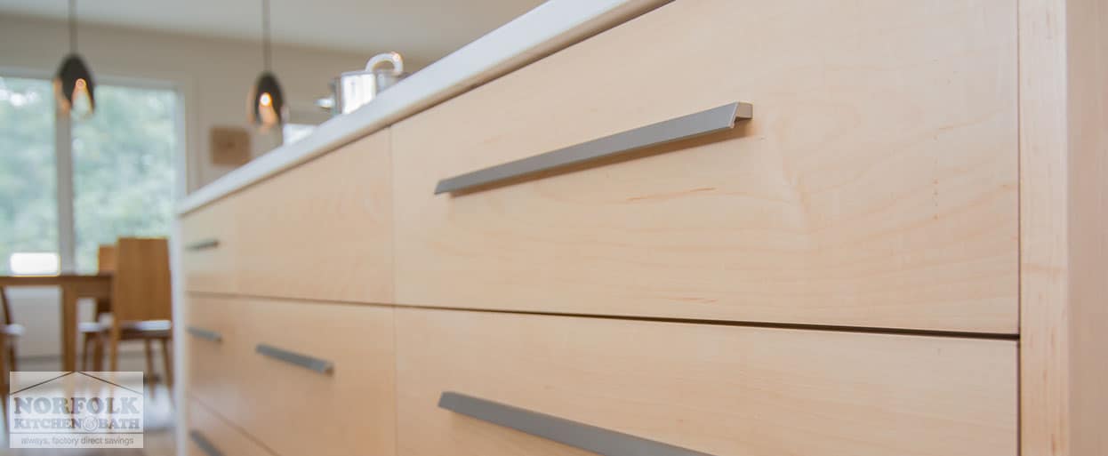 close up of full-access base kitchen cabinets, in a natural finish, with long modern cabinet hardware