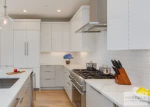 All white kitchen with white tile, white cabinets and white counterops and hardwood floors