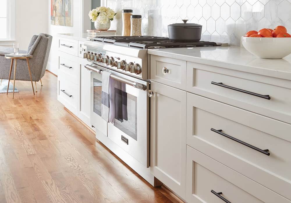 white kitchen cabinets with modern bar hardware and a gas range