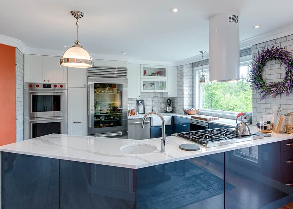 a modern kitchen with blue and white kitchen cabinets, double ovens, a glass refrigerator and countertop range.