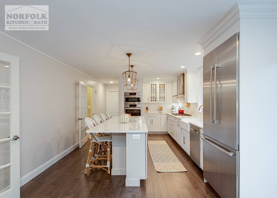 side view of a large white kitchen with an island featuring gold accents and stainless steel appliances