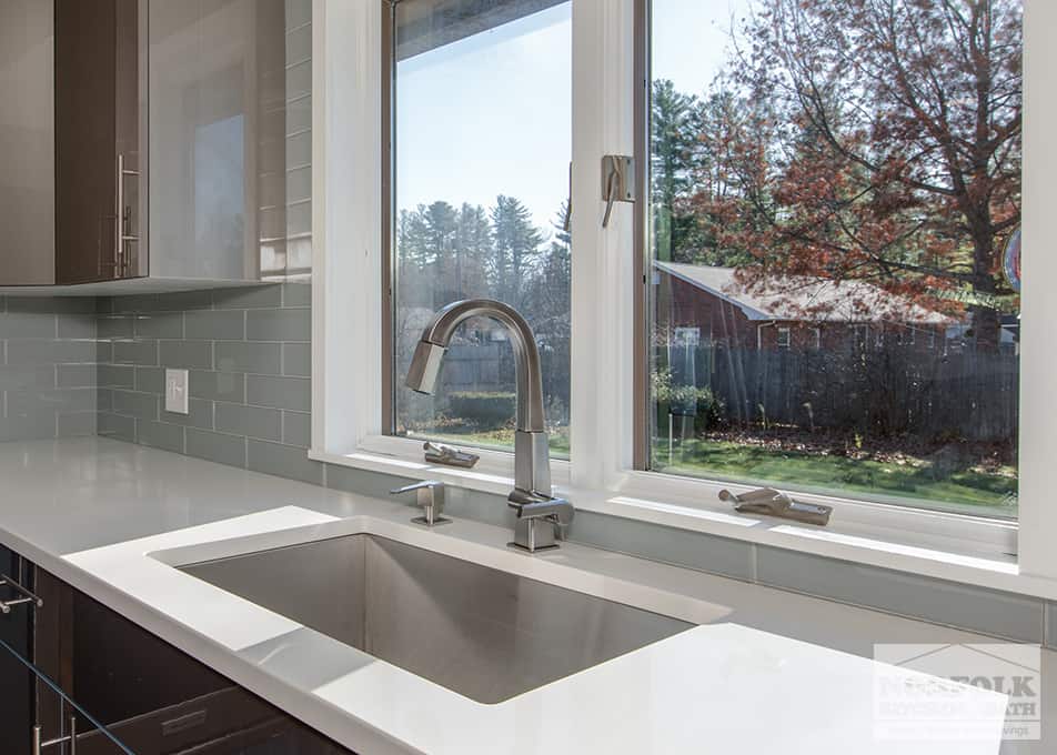 close up of a stainless steel undermount kitchen sink with a pull down faucet in front of a window leading to the backyard