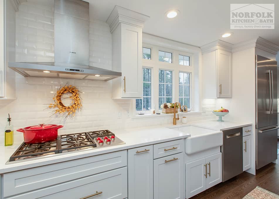 white kitchen cabinets with a gas cooktop, stainless steel range hood and a white apron sink with gold faucet and cabinet hardware