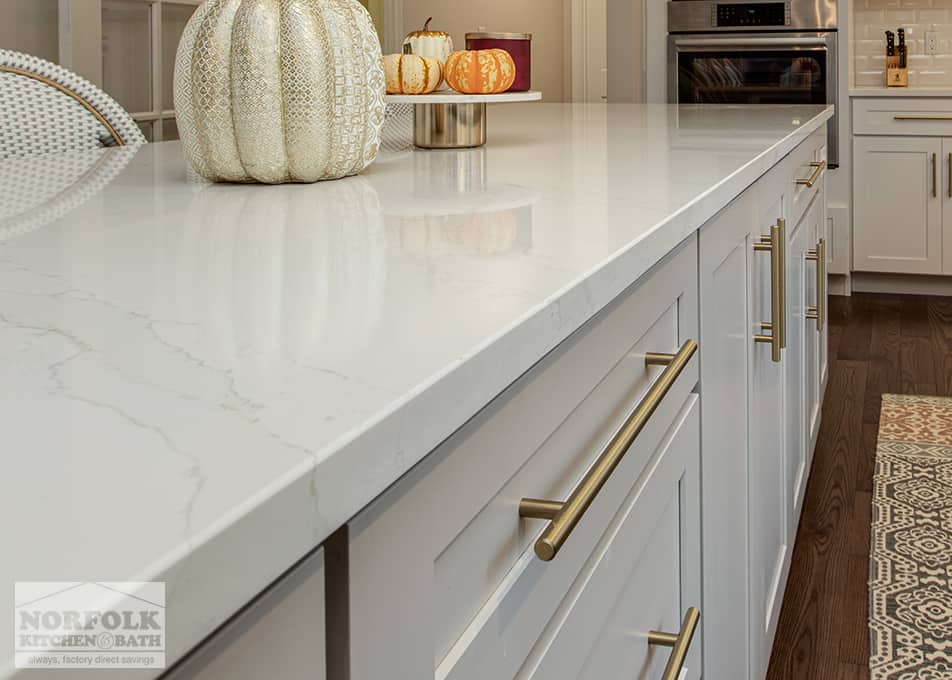 close up of a white quartz countertop on top of kitchen cabinets with modern gold hardware