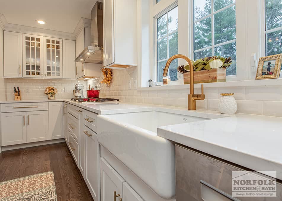 close up, angled view of a white apron sink with gold faucet in a white kitchen