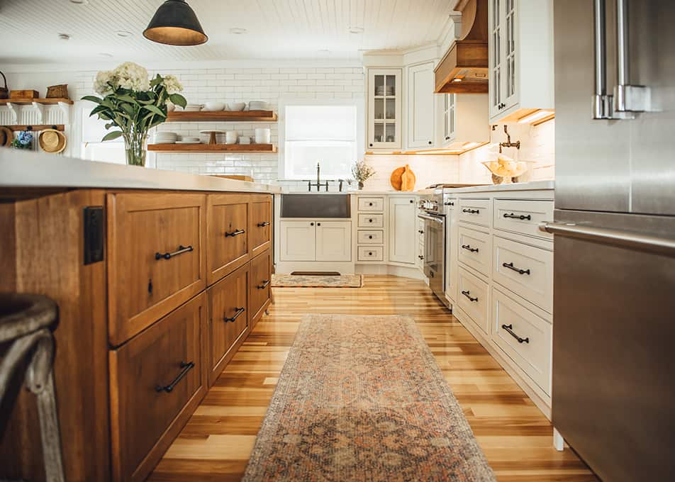 low shot of a kitchen runway with warm woodgrain cabinets on the left and modern white cabinets on the right with a stainless steel apron sink at the end