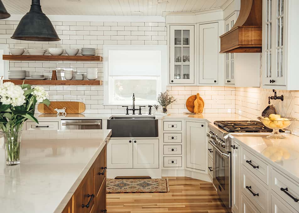 a modern farmhouse white kitchen with a hickory kitchen island, matching floating shelves and range hood, and white subway tile to the ceiling
