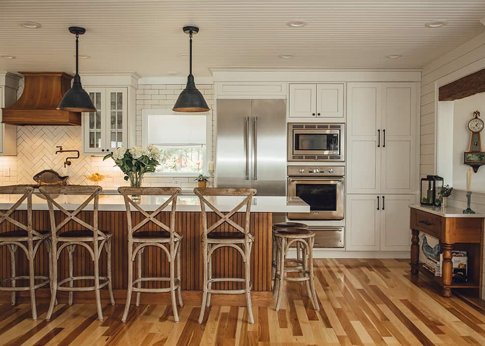a large white L-shaped kitchen with stainless steel appliances and a large woodgrain island with bar stools