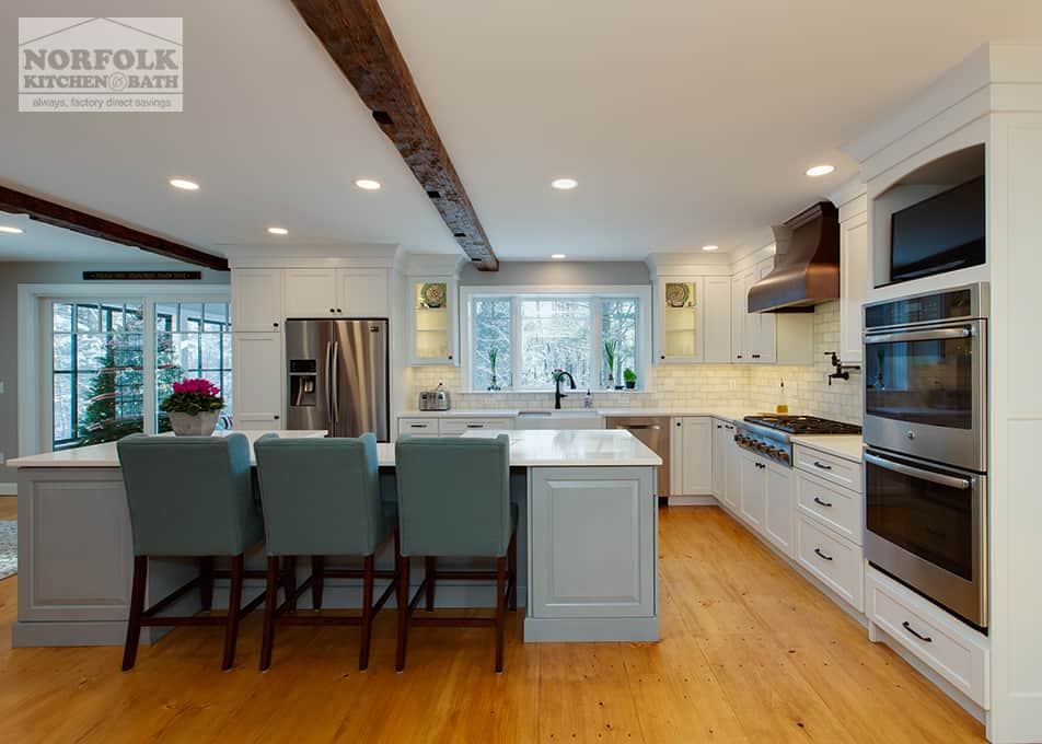 an  L-shaped white kitchen with a large grey furniture-style island, green backed bar stools, stainless steel appliances & a copper range hood.