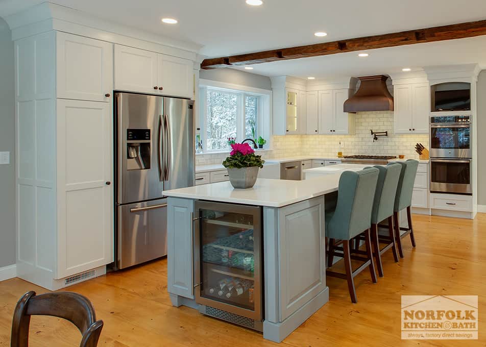 an  L-shaped white kitchen with a large grey furniture-style island with a beverage fridge on the end, green backed bar stools, stainless steel refrigerator & a copper range hood.