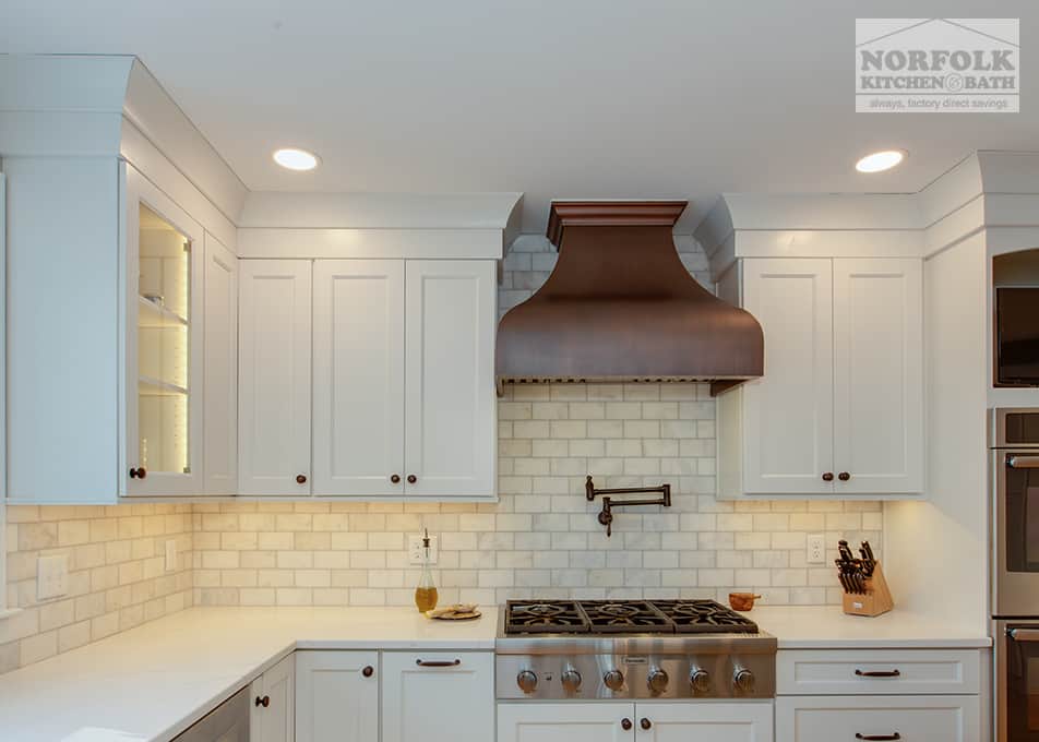 close up of white cabinets with a gas range stove, pot filler and a custom copper hood 