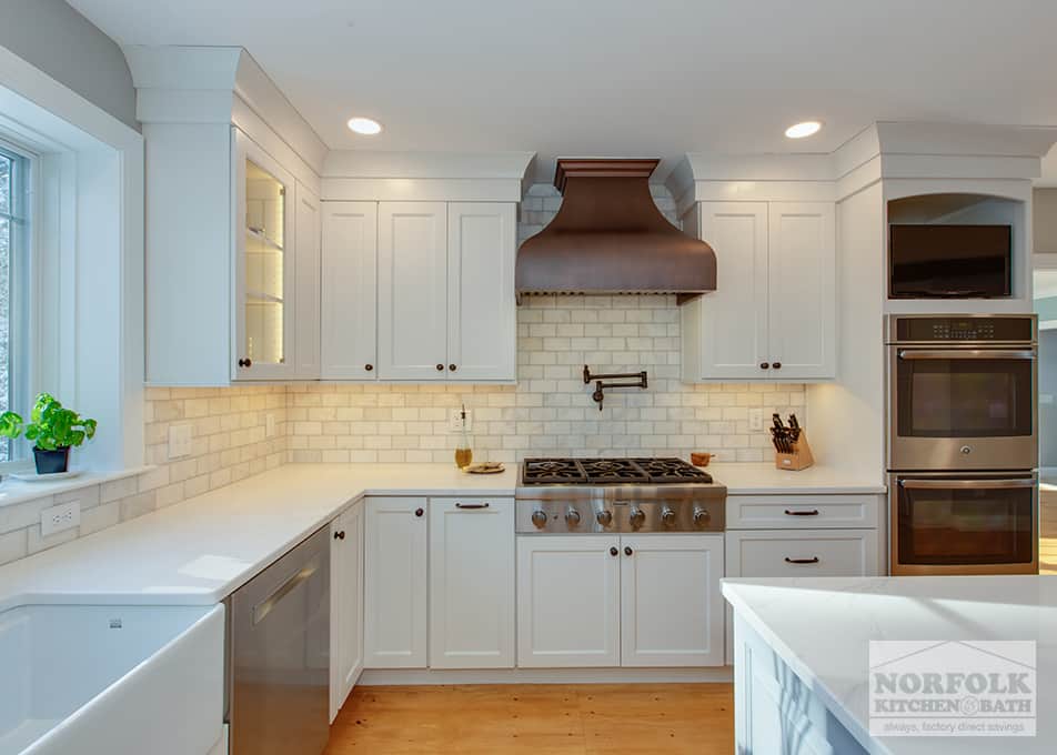 an L-shaped white kitchen with a gas range stove and a custom copper hood