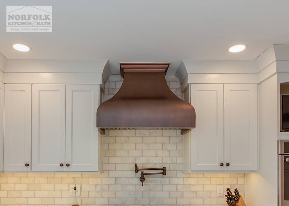 close up of a copper range hood next to white kitchen cabinets