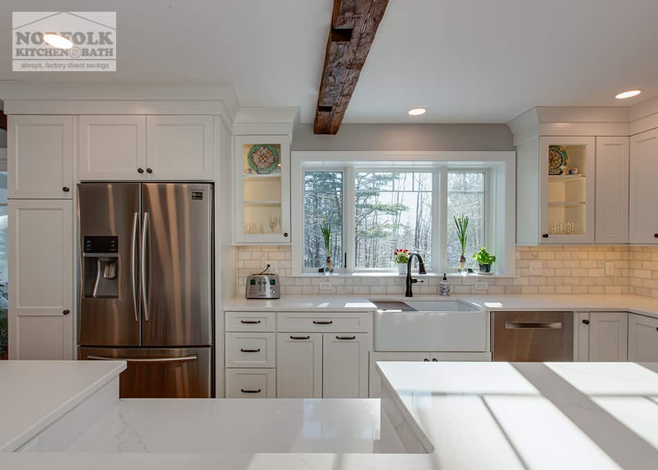 a white kitchen with a dual-level island in front, a stainless steel refrigerator, a white apron sink, and a wooden beam in the middle of the ceiling