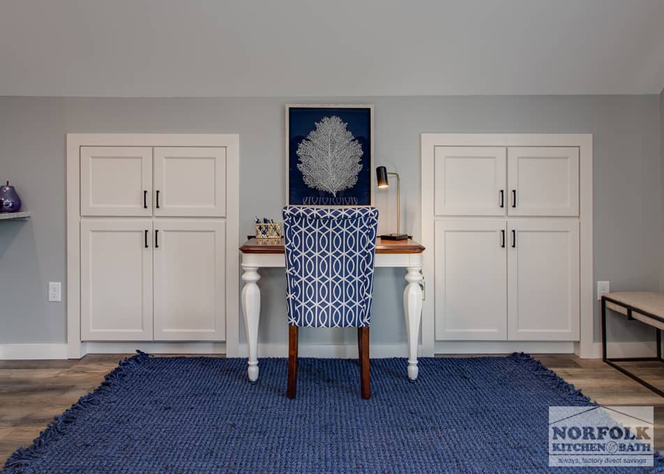 a small desk with a blue fabric chair & rug, and white built ins on either side