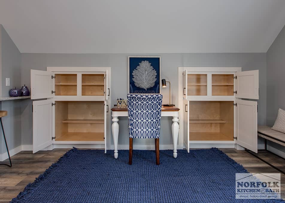 a small desk with a blue fabric chair & rug, and white built ins on either side with the doors opened