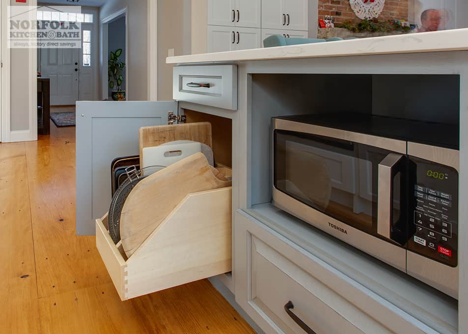 gray kitchen cabinets with a built-in microwave and an open cabinet with a cutting board organizer