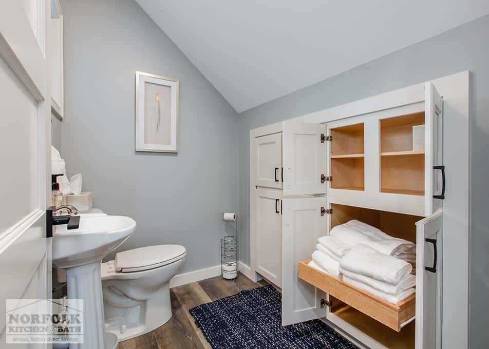 a small angled bathroom with white built in's with one opened to show a drawer full of towels and linens