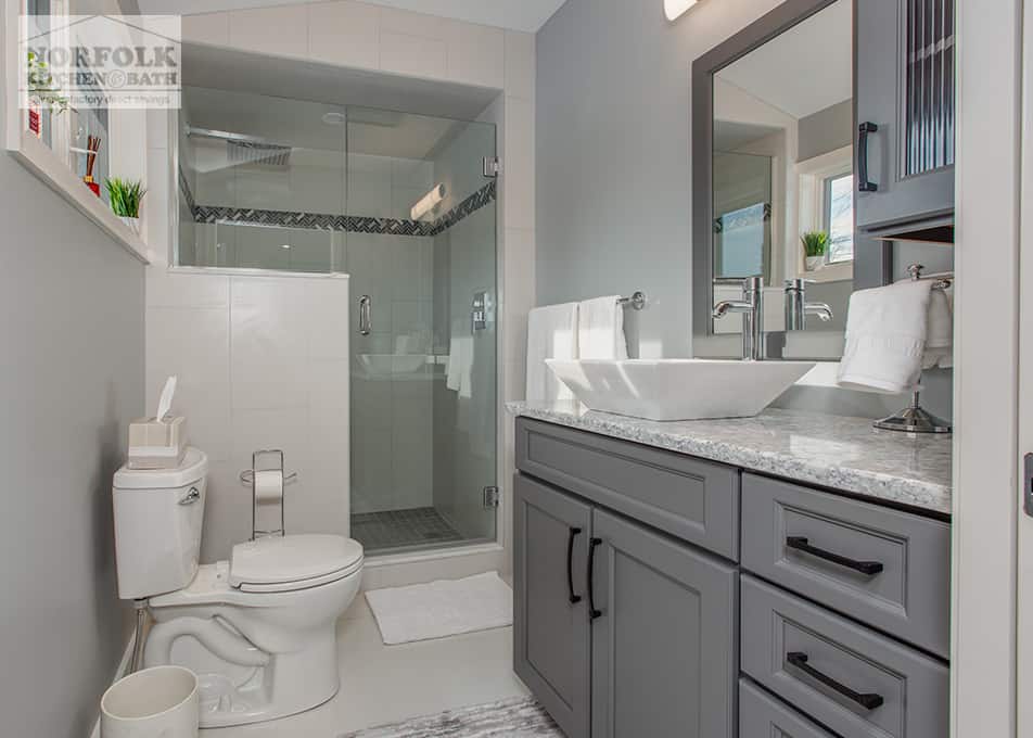 a master bathroom with a dark gray vanity, bowl sink and glass enclosed shower