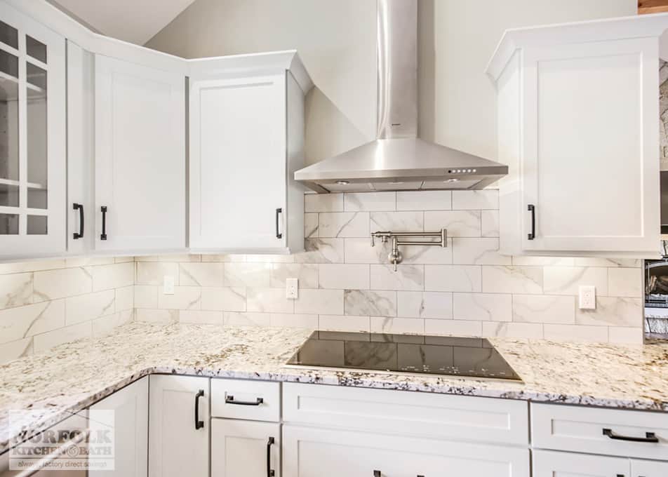 close up of an electric stove insert and a stainless steel hood with pot filler next to white kitchen cabinets