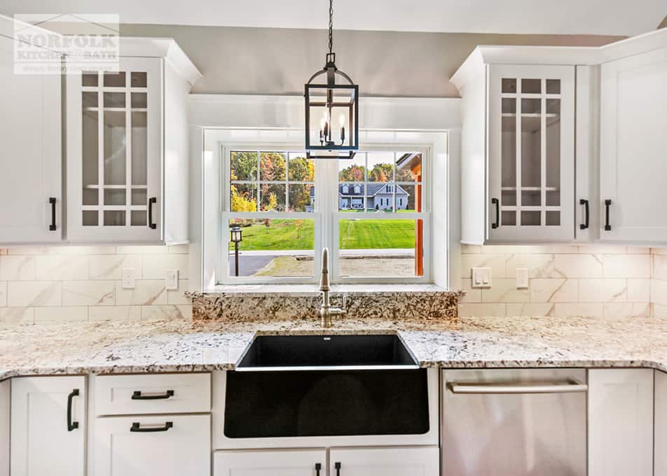 close up of a black stainless farmer's sink in a kitchen with white cabinets and granite countertops