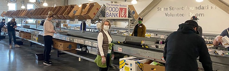 a group of people standing around a conveyor belt organizing food donations at Greater Boston Food Bank