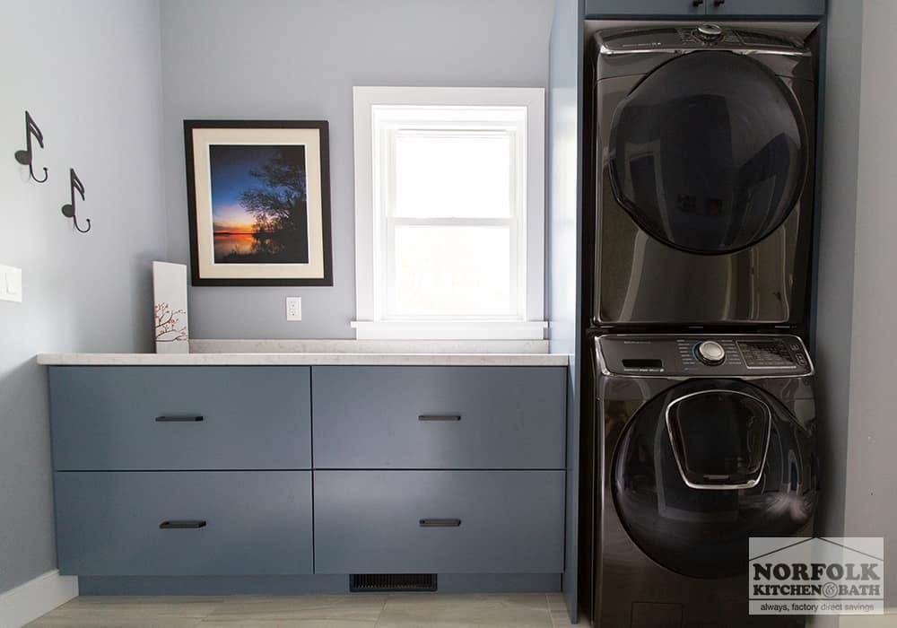 laundry room with blue base cabinets, black hardware and black stainless washer and dryer stacked on each other