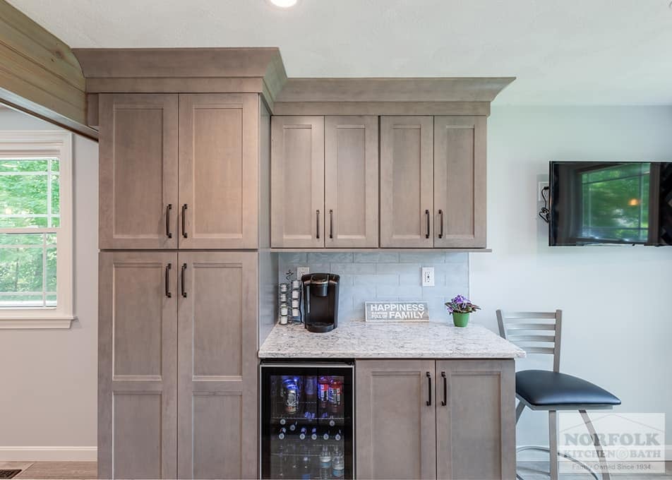 custom bar area in a Wilmington kitchen remodel with shaker cabinets in a gray stain, white stone countertop and a Keurig and wine fridge with a TV mounted on the wall to the right