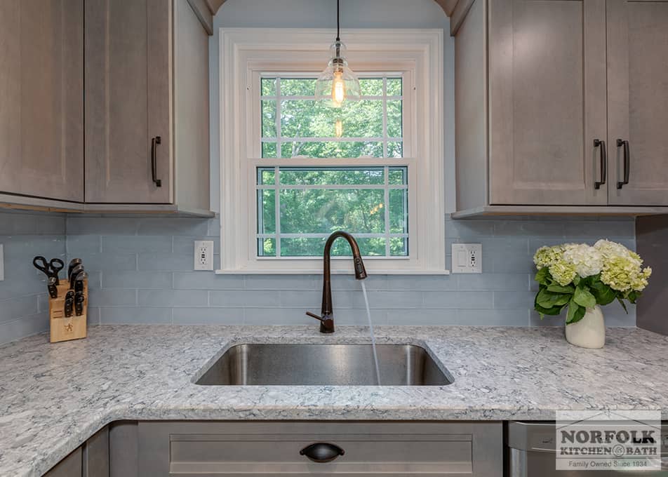 close up of a kitchen sink inside a Wilmington, MA kitchen remodel featuring gray stained cabinets and white stone countertops