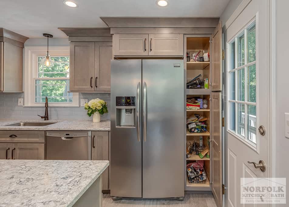 a Wilmington, MA kitchen remodel featuring gray stained cabinets and a large pantry cabinet to the right of the fridge, open with multiple things stored on shelves inside