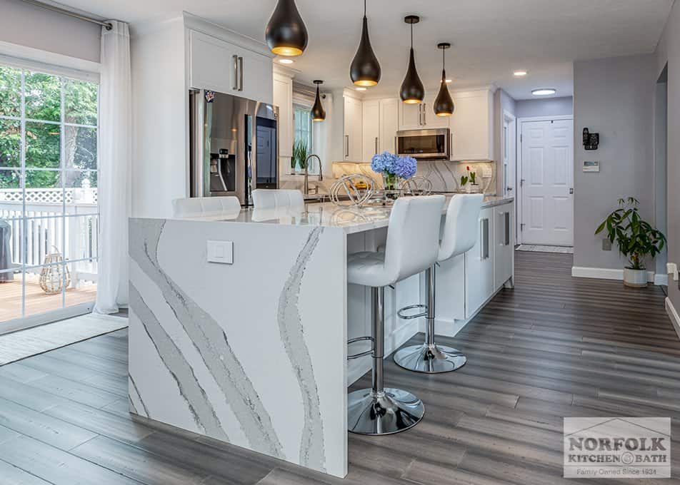 a kitchen featuring white slim shaker cabinets, white and gray quartz countertops and a waterfall edge on the island