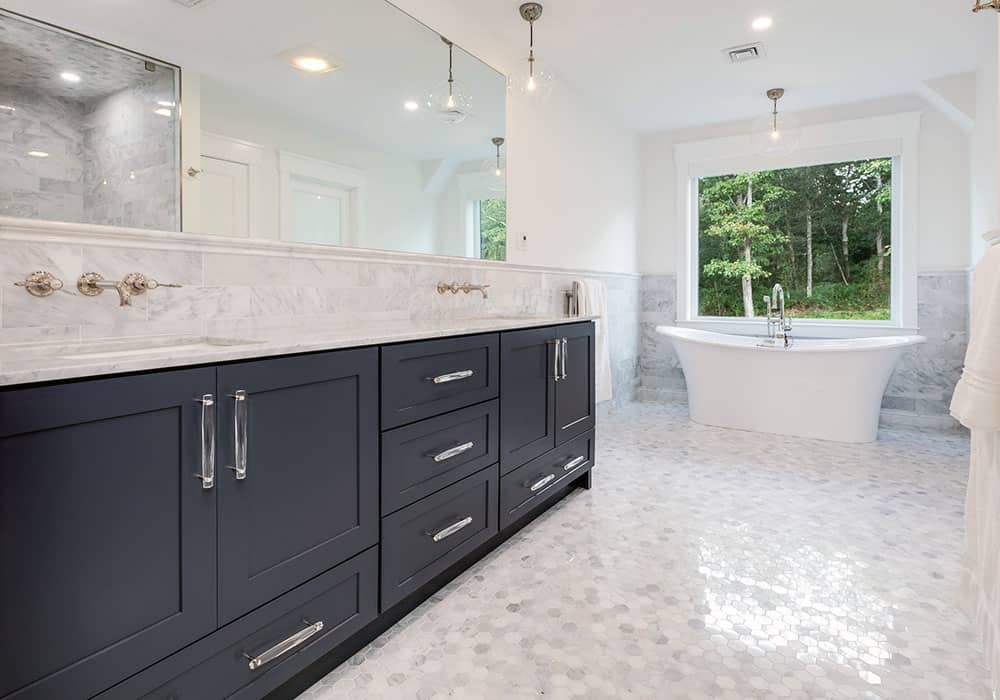 a modern bath remodel with navy blue double vanity, stone countertops and a standalone tub
