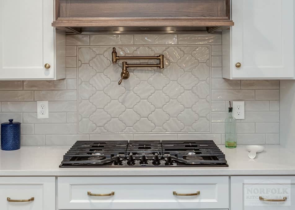 close up of white glass tile behind a stove in a white kitchen