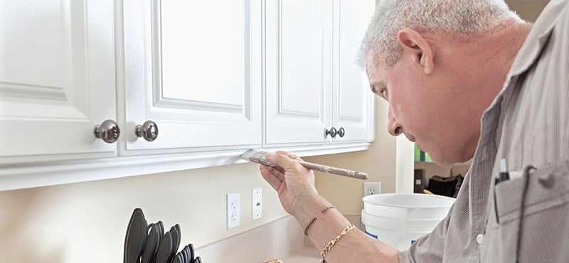 a man painting his cabinets white
